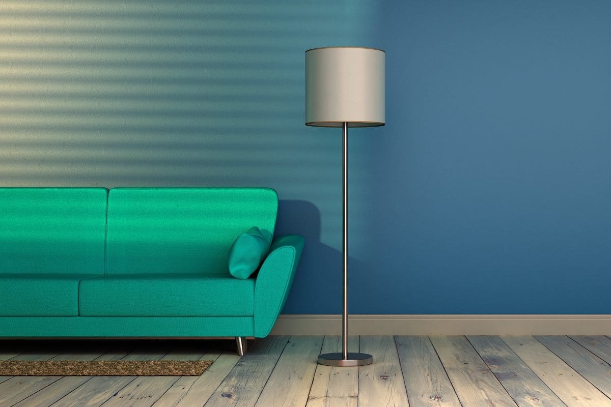 Zielona sofa przy niebieskiej ścianie z lampą stojącą w salonie